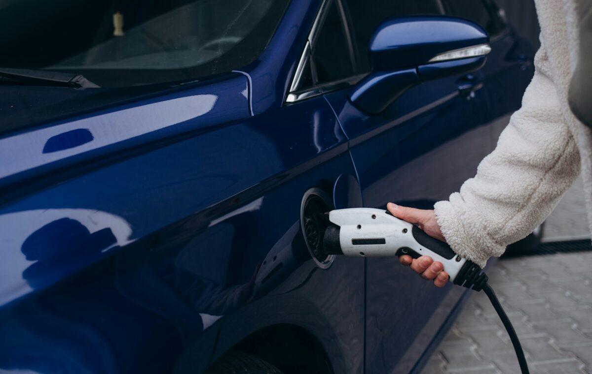Human hand is holding Electric Car Charging connect to Electric car
